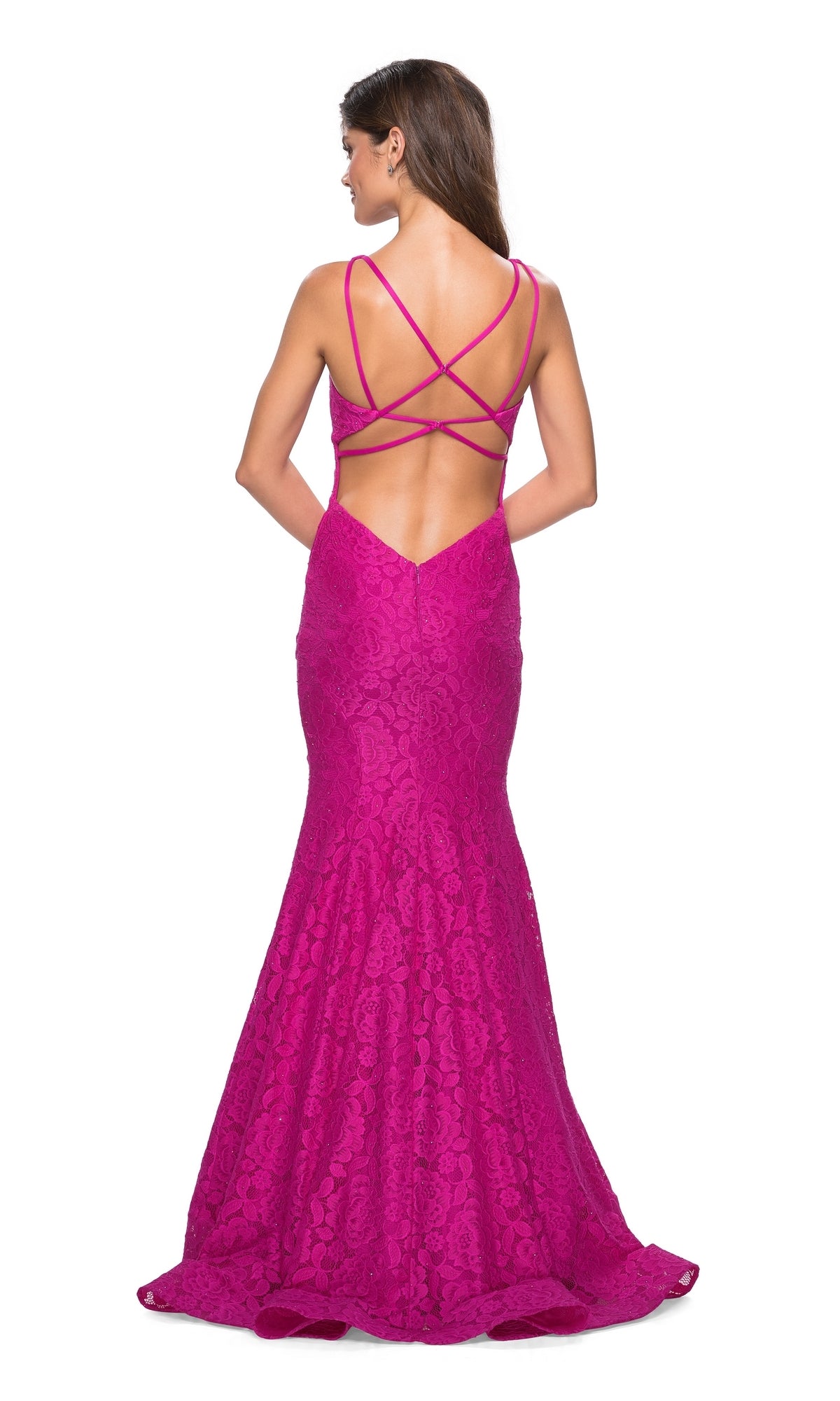 A woman stands with her back to the camera, wearing the floor-length magenta La Femme 27623 Open-Back Lace Mermaid Prom Dress featuring crisscross straps and elegant lace detailing.